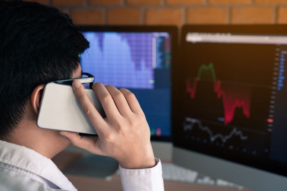 Trader talking into phone while looking at trading analysis